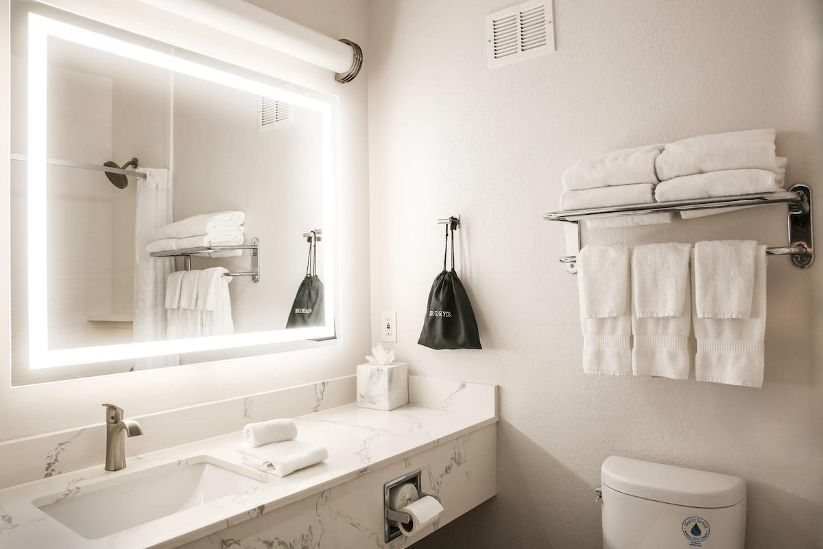 Une salle de bain avec un grand miroir, un lavabo doté d’un plan de travail en marbre, un porte-serviettes avec des serviettes pliées et des toilettes.