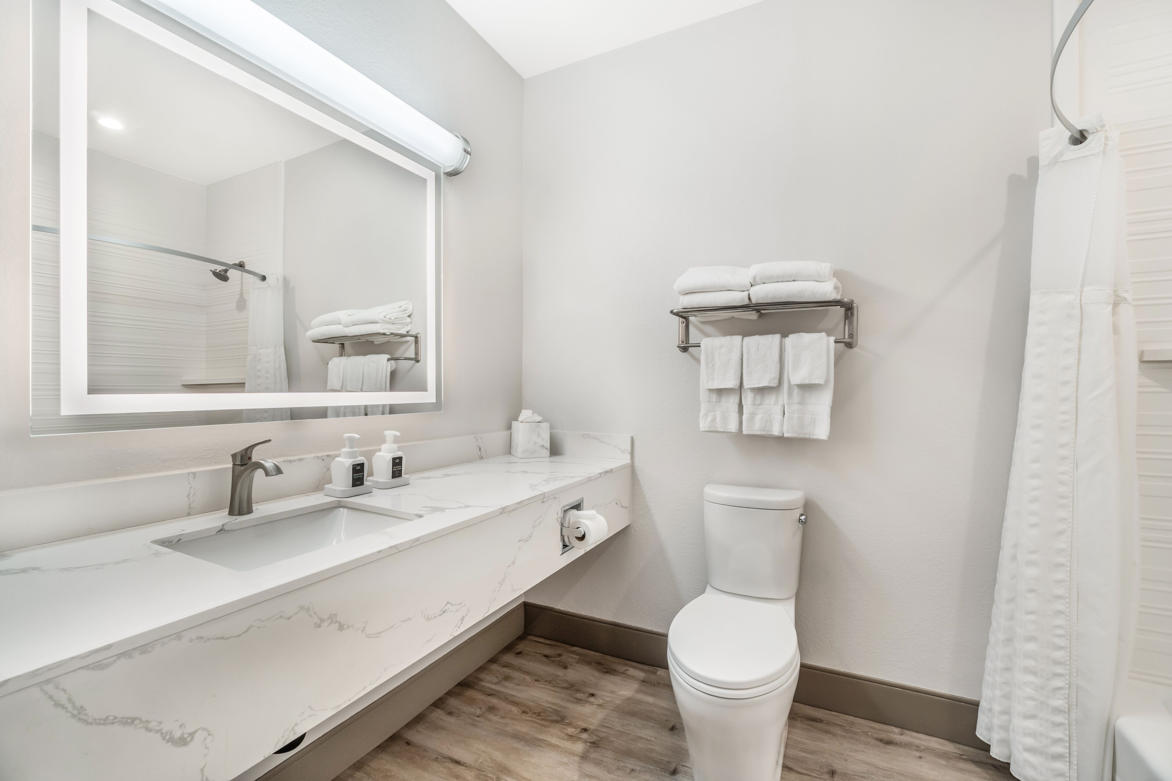 A modern bathroom with a marble countertop, a toilet, a towel rack, and a shower curtain.