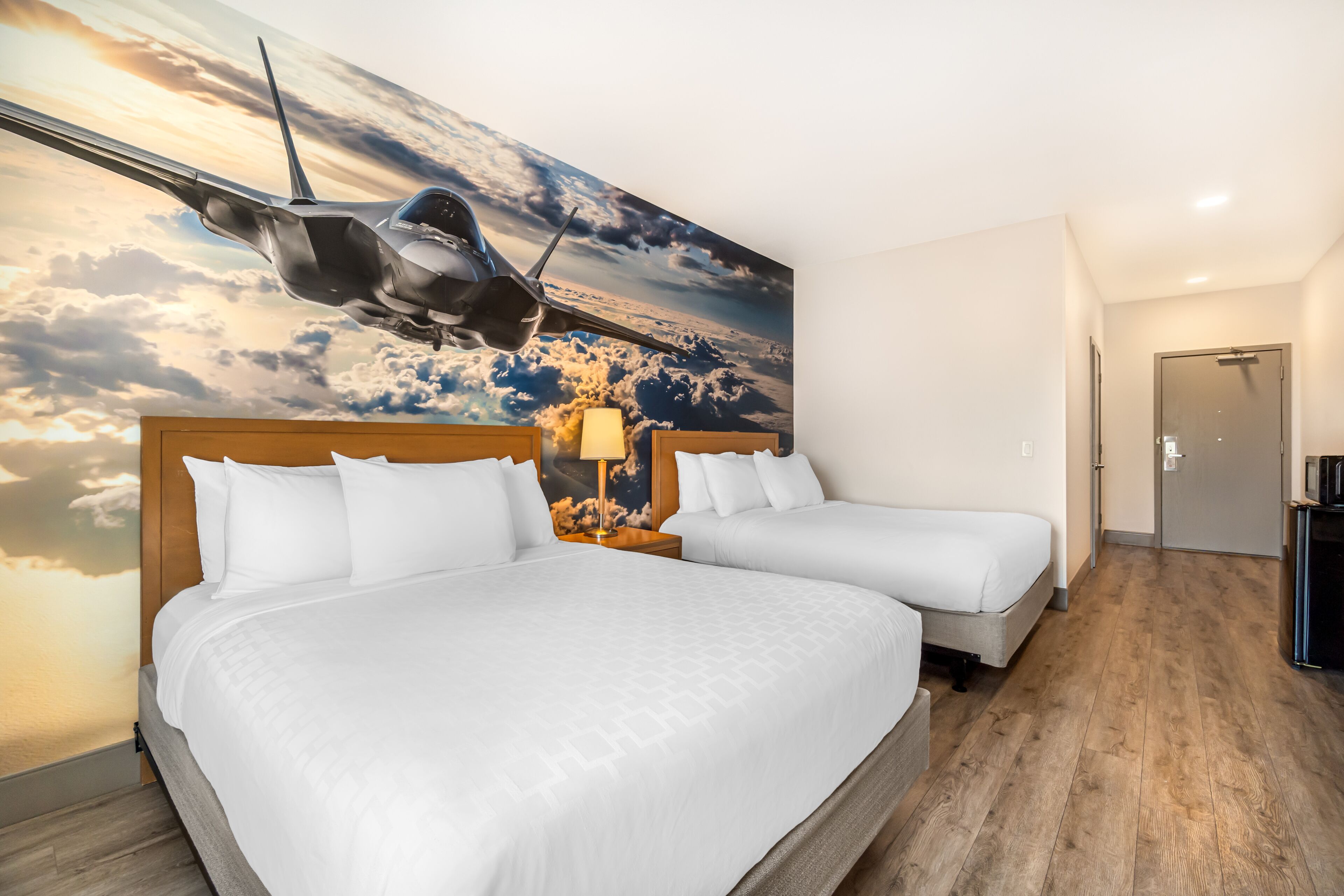 Ein Hotelzimmer mit zwei Betten, einem großen Wandgemälde mit einem Flugzeugmotiv und einem Holzboden.