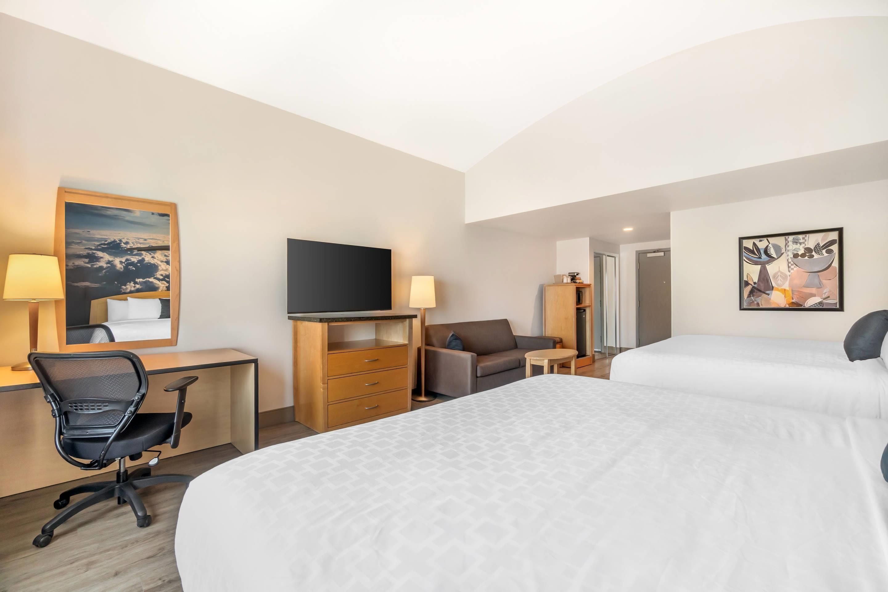 A hotel room with a bed, desk, chair, television, and artwork on the walls.