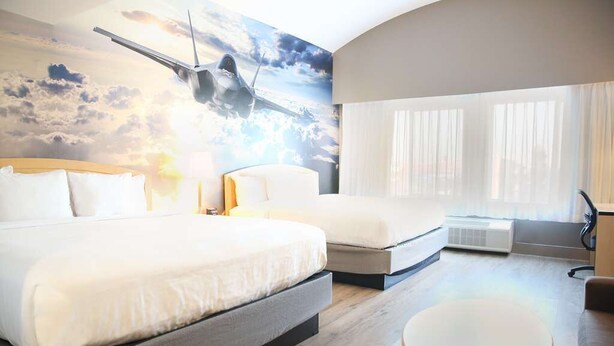 A hotel room with a large bed, a smaller bed, a round table, and a mural of an airplane.
