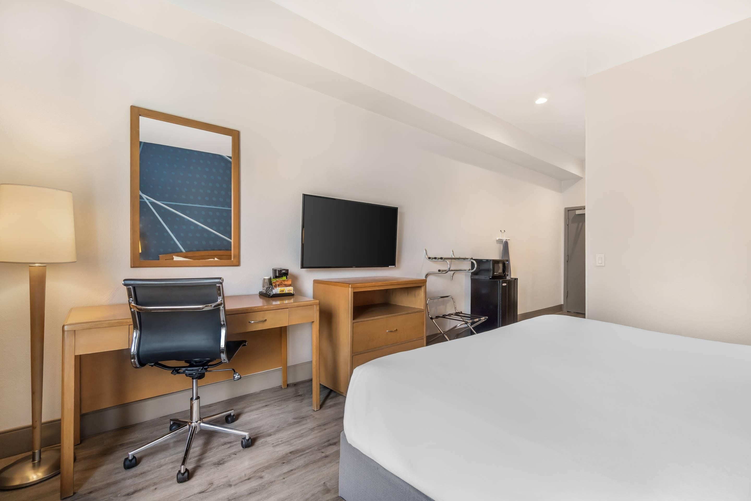 Ett hotellrum med en säng, ett skrivbord, en stol, en tv och ett litet pentry.