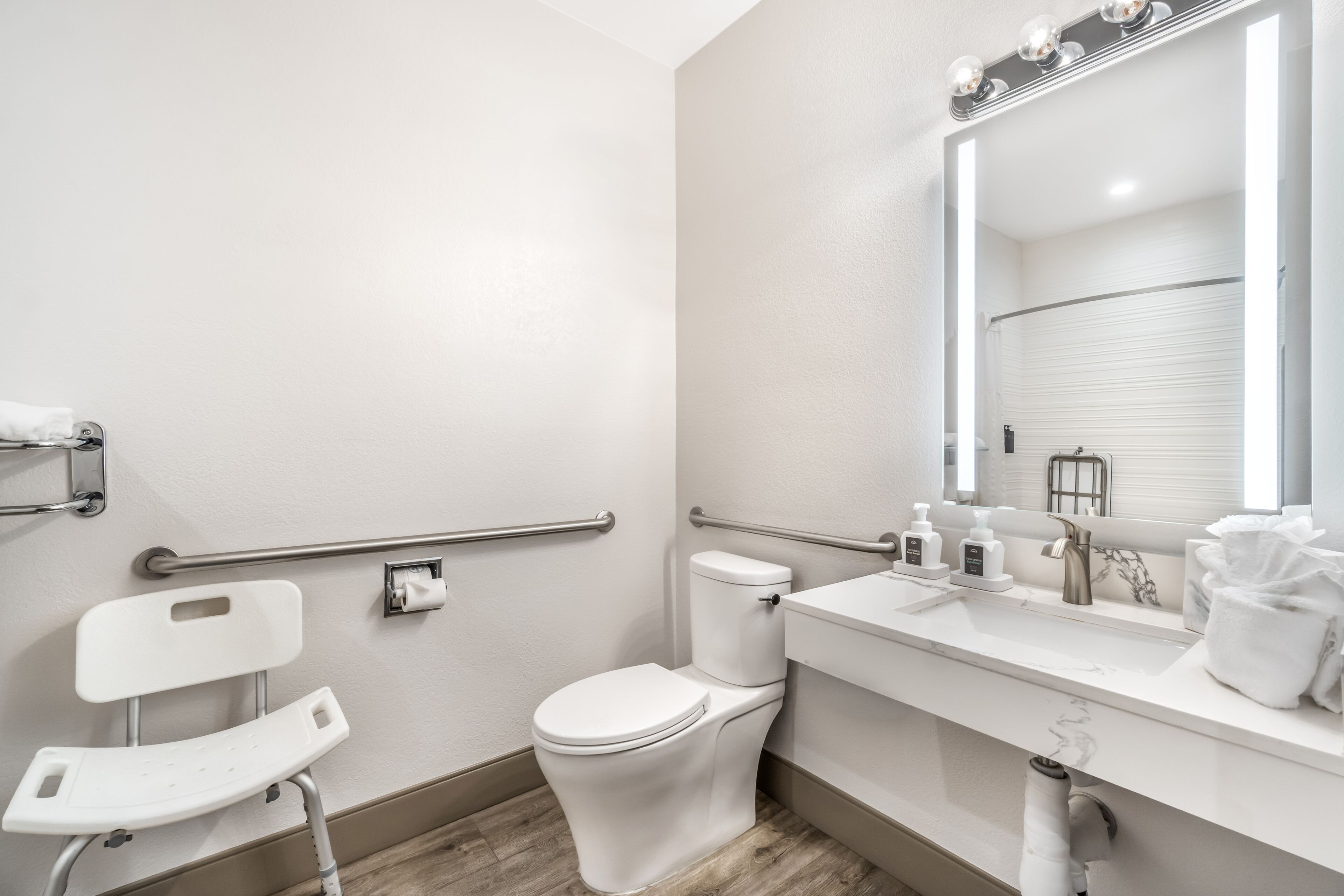 Et moderne badeværelse med toilet, vaskebord med spejl og gelænder for tilgængelighed.