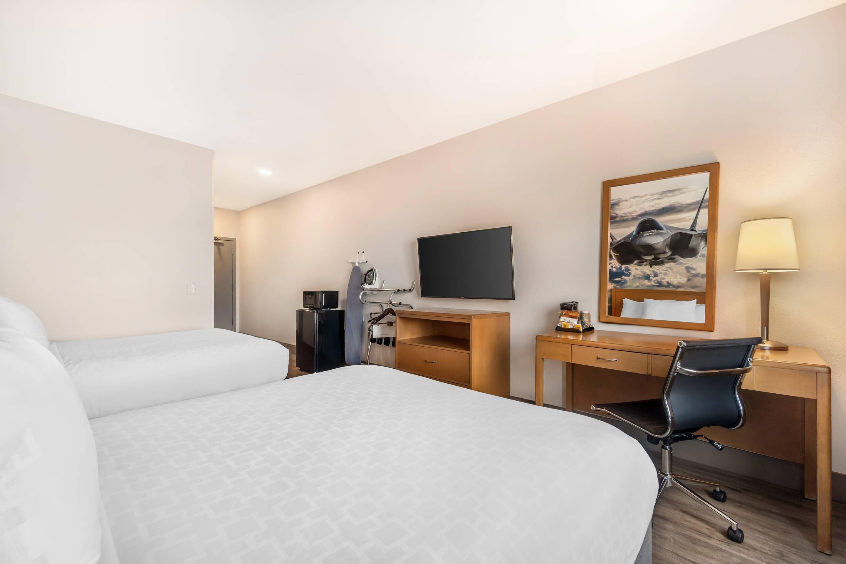 Een hotelkamer met twee bedden, een bureau met een televisie, een stoel, een bureaulamp en een schilderij aan de muur.