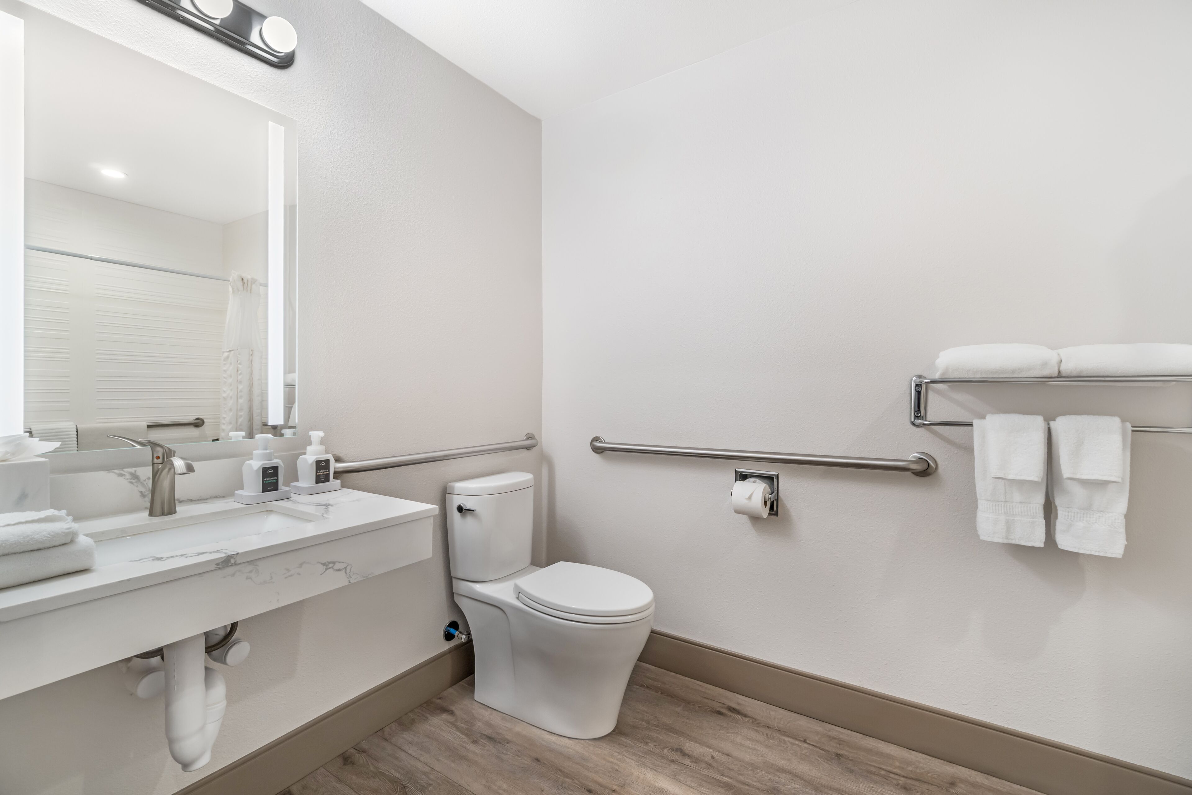 Un baño moderno con inodoro, lavamanos, espejo y barras de apoyo.