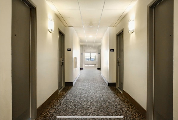 A hotel hallway with carpeted floors, doors numbered 307 and 308, and wall-mounted light fixtures.