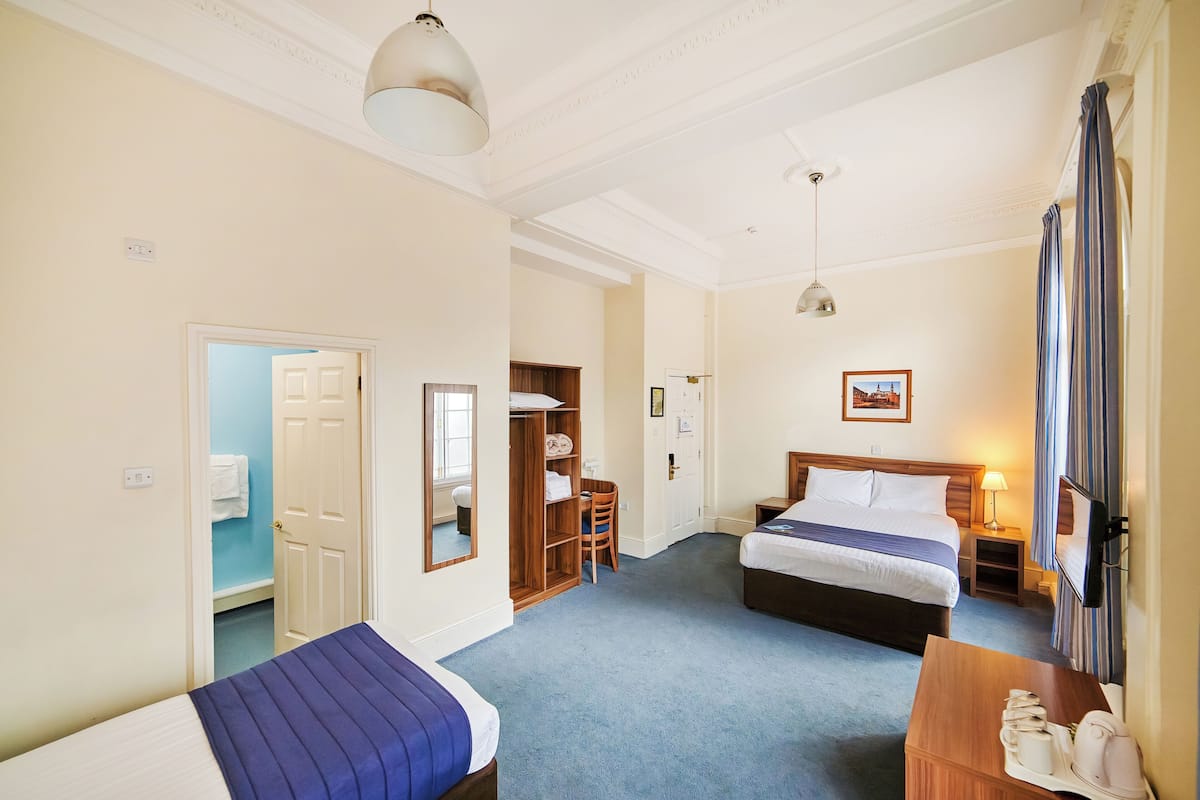 A hotel room with two beds, a wooden wardrobe, a desk with a lamp, and a television.
