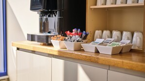 Una estación de café con varias cafeteras y una máquina de café, junto con recipientes con cápsulas de café y un portaletras con etiquetas.