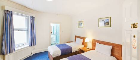 A hotel room with two beds, a window with curtains, a radiator, and a door with the number 705.