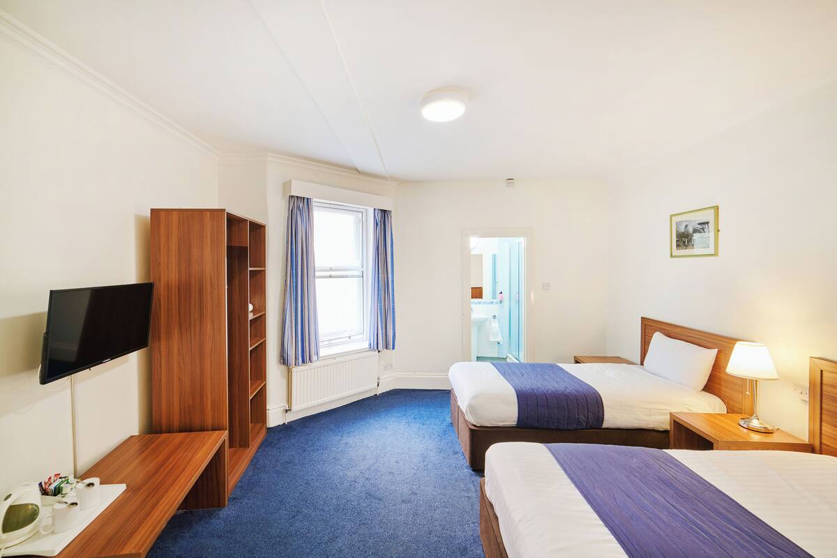 A hotel room with two beds, a TV, a wooden wardrobe, and a bathroom visible through a door.