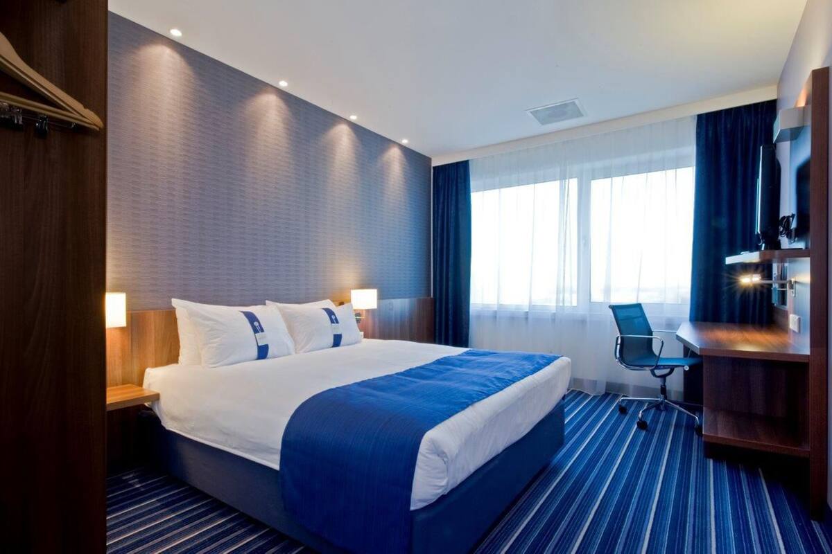 A hotel room with a large bed, a desk, and a chair.