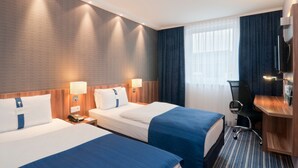 A hotel room with two beds, a desk, a chair, a TV, and a window with curtains. - Holiday Inn Express London - Vauxhall Nine Elms by IHG (London)