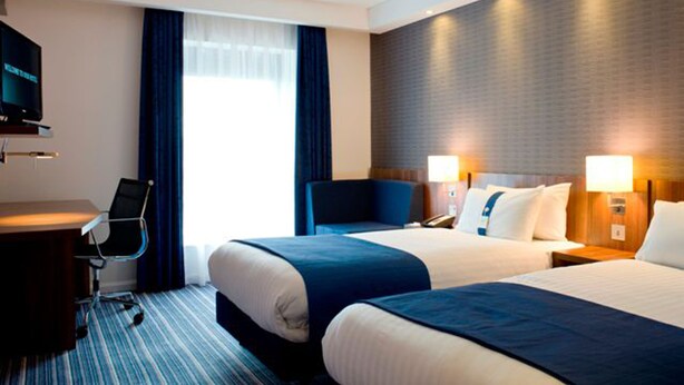 A hotel room with two beds, a desk, a chair, a television, and a large window with curtains. - Holiday Inn Express London - Vauxhall Nine Elms by IHG (London)