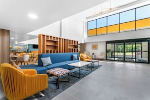 Um lobby moderno com um sofá azul, poltronas amarelas e uma estante de madeira.
