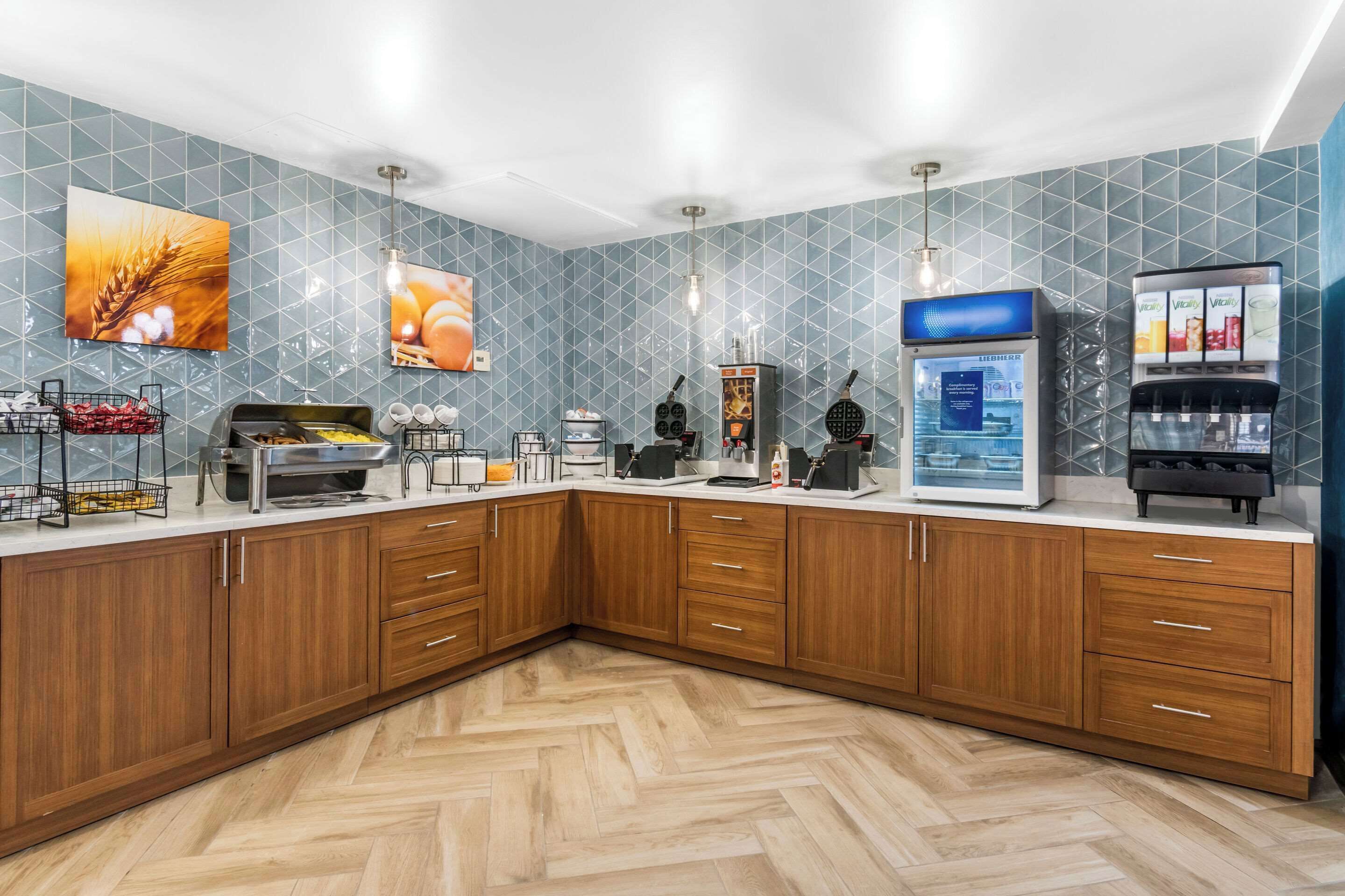 A modern kitchen with wooden cabinets, a herringbone floor, and a blue tiled backsplash.