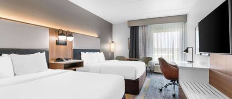 A hotel room with two beds, a desk, a chair, a TV, and a window with curtains.