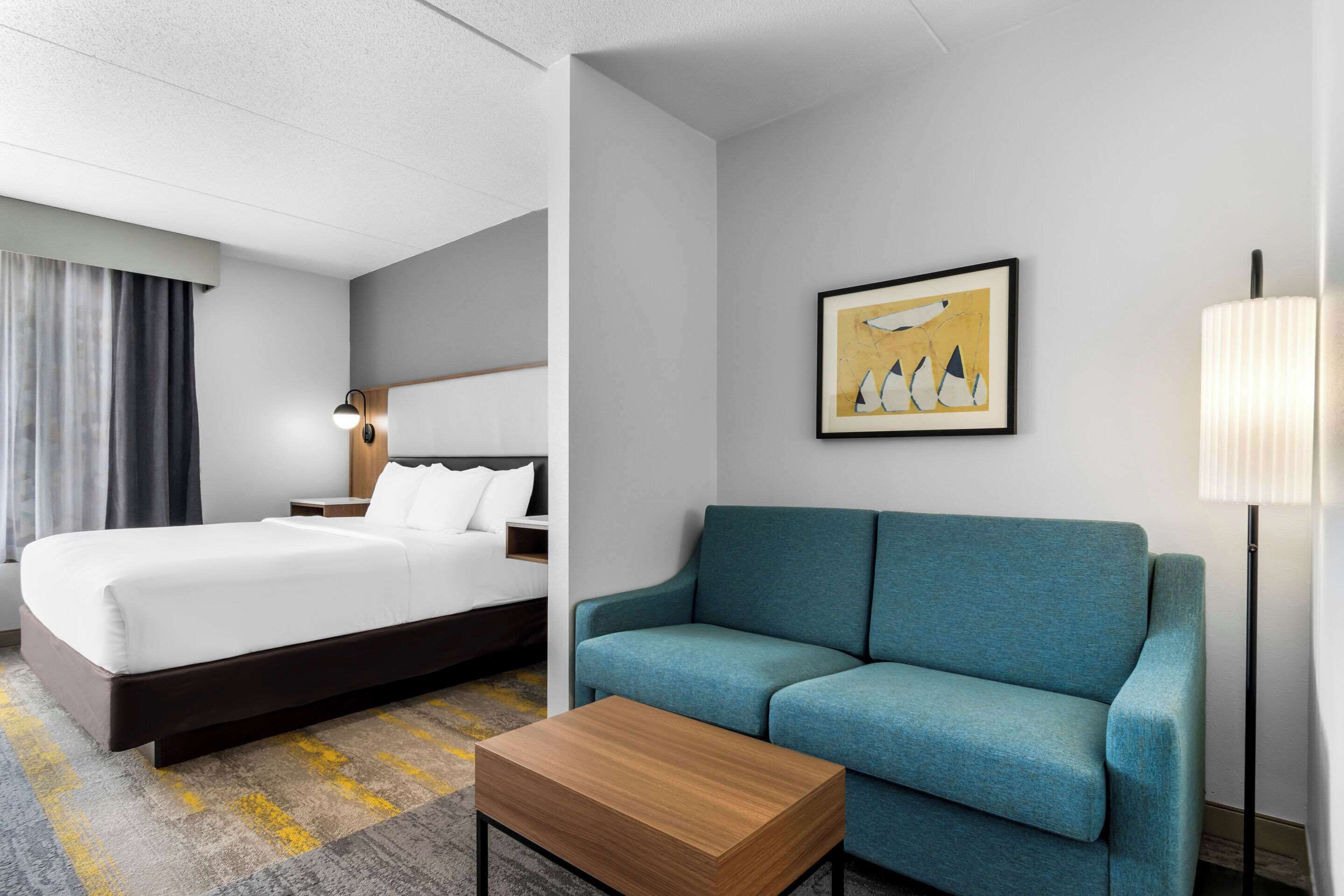 A hotel room with a bed, a sofa, a coffee table, and a lamp.