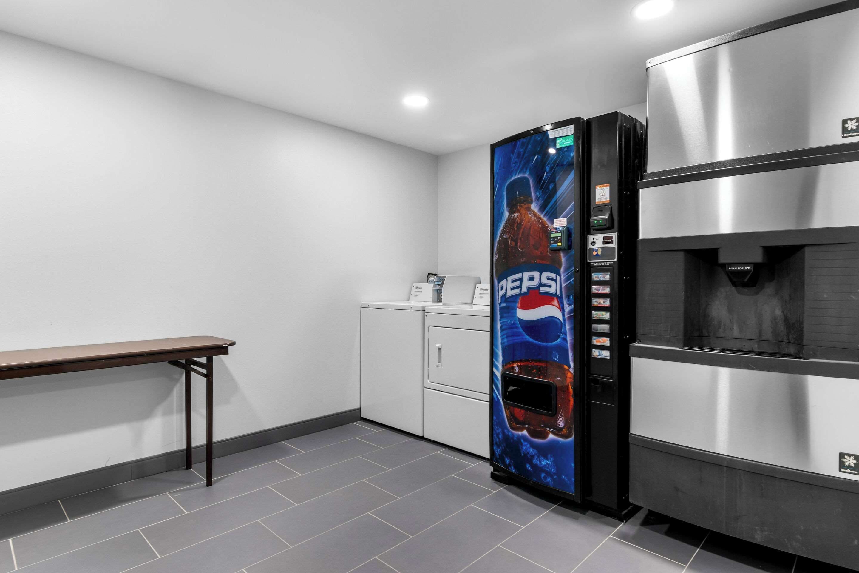 A kitchen with a stainless steel refrigerator, a vending machine, a white cabinet, and a wooden bench.