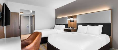 A hotel room with two beds, a desk, a chair, and a TV.
