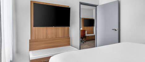 Een moderne hotelkamer met een groot bed, een houten kledingkast, een flatscreen televisie, een bureau en een stoel.