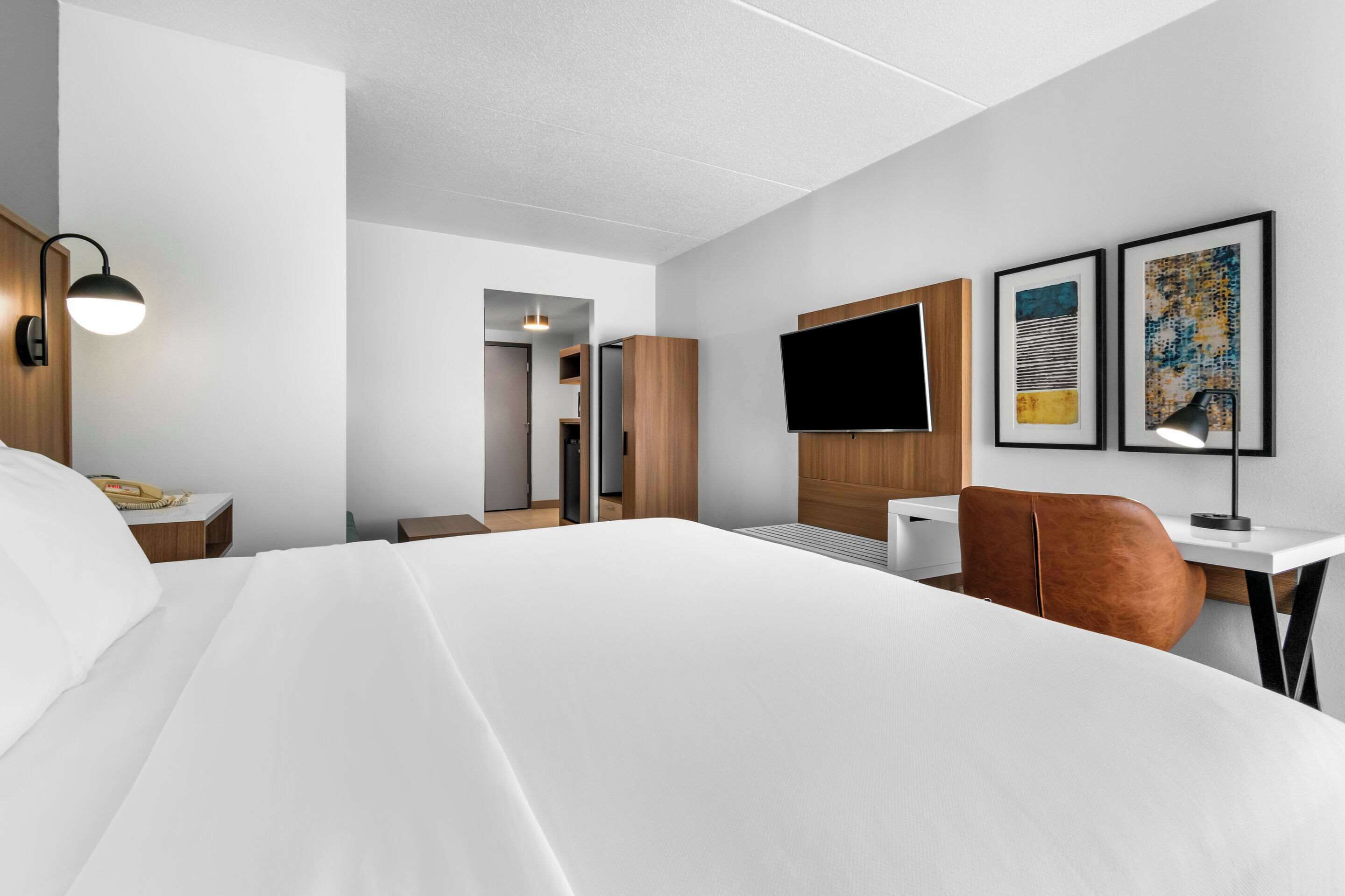 A modern hotel room with a large bed, a desk with a chair, a flat-screen TV, and artwork on the walls.