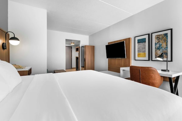 Quarto de hotel moderno com uma cama grande, uma escrivaninha com cadeira, televisão de tela plana e obras de arte nas paredes.