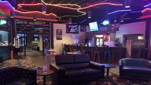 A bar area with leather seating, a patterned carpet, and neon lighting.