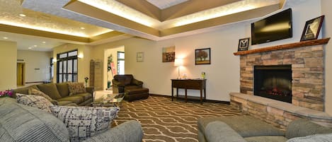 A spacious living room with a fireplace, comfortable seating, and a television mounted above it.