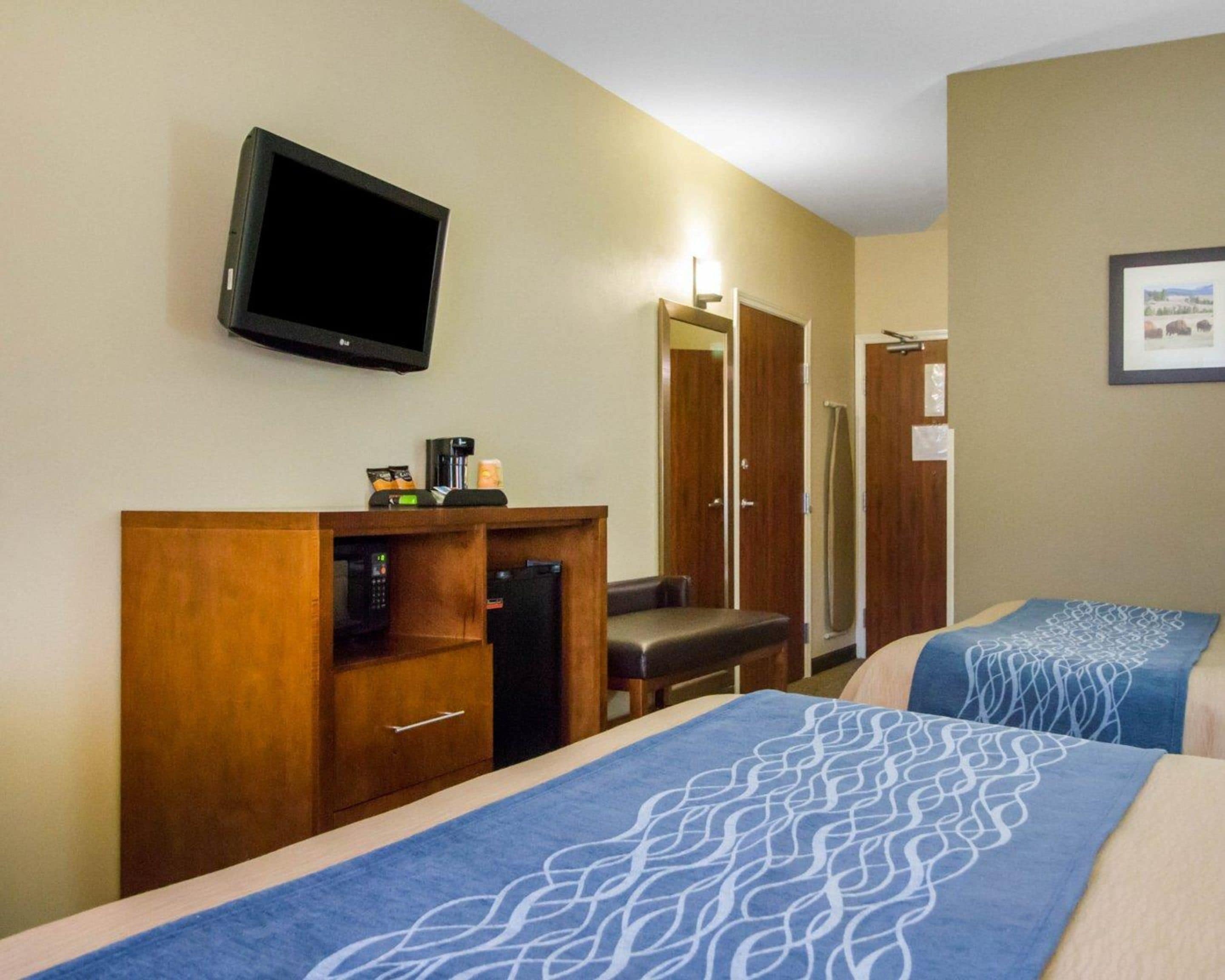 A hotel room with two beds, a TV, a coffee maker, and a mirror.