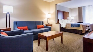 A hotel room with a blue sofa, a wooden coffee table, a bed with a white headboard, and two bedside lamps.