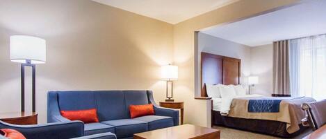 A hotel room with a blue sofa, a wooden coffee table, a bed with a white headboard, and two bedside lamps.