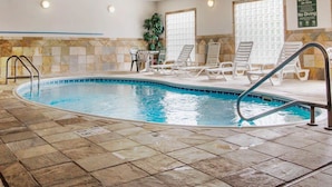 An indoor swimming pool with tiled walls, lounge chairs, and a sign indicating pool rules.