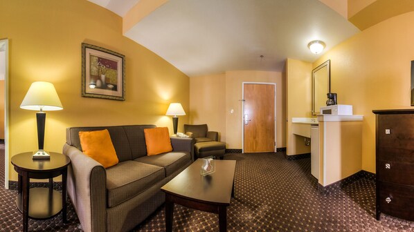 A hotel room with a sofa, two lamps, a coffee maker, a small table, and a door leading to a bathroom.