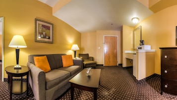 A hotel room with a sofa, two lamps, a coffee maker, a small table, and a door leading to a bathroom.