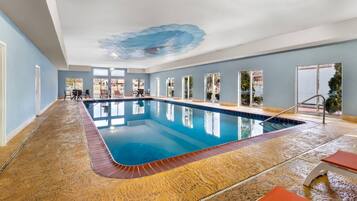An indoor swimming pool with clear blue water, surrounded by a tiled floor, and a ceiling mural.