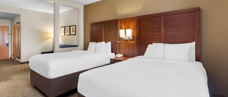 Habitación de hotel con dos camas, cabecero de madera, mesita de noche con lámpara y suelo alfombrado.