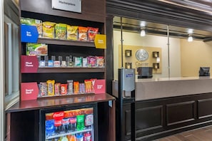 A hotel reception area with snack and ice box shelves, a refrigerator with beverages, and a counter with a clock and a sign reading "Comfort". - Comfort Suites Goodlettsville Rivergate (Goodlettsville)