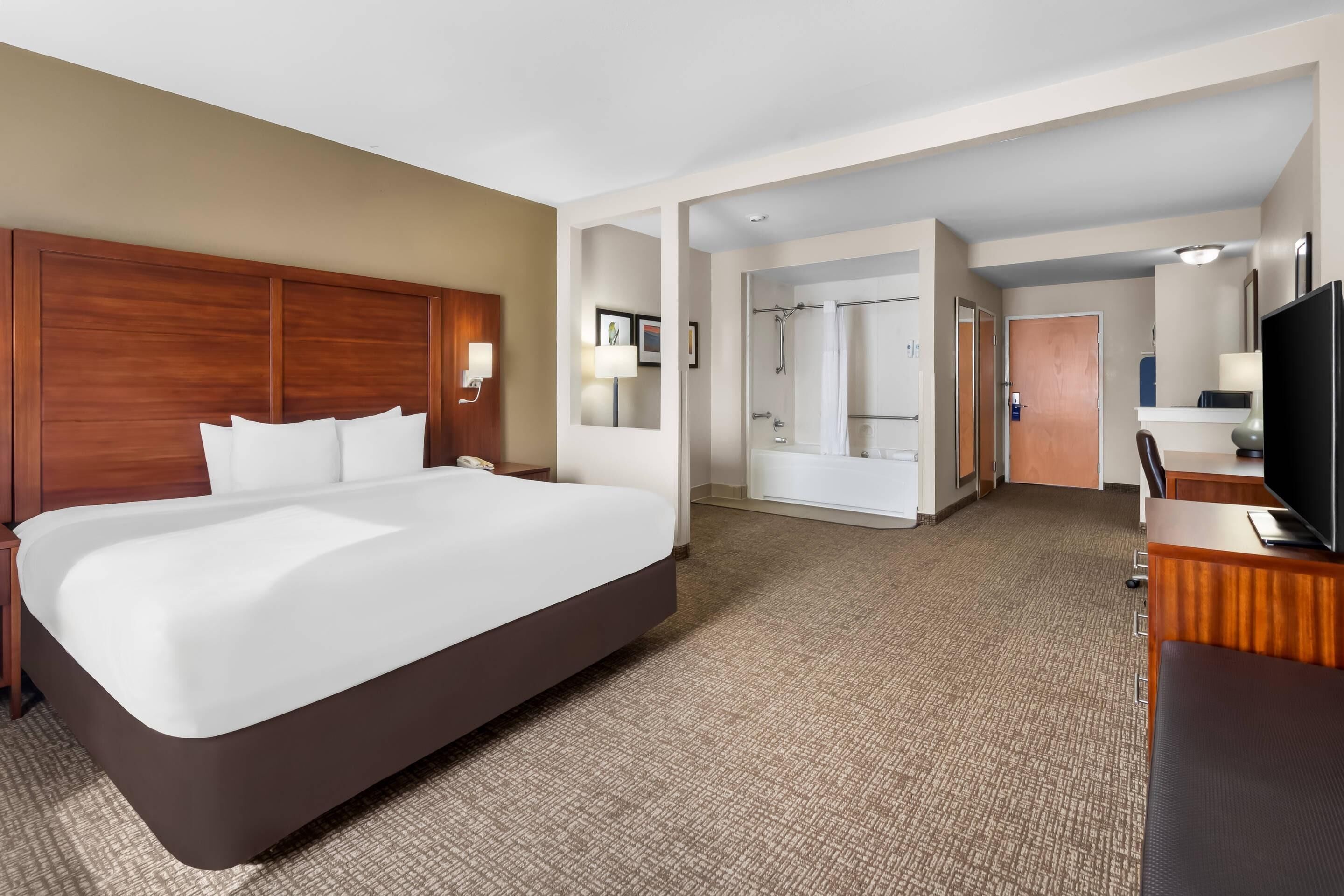A hotel room with a large bed, a desk, a TV, a bathroom, and a shower.