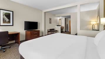 Une chambre d’hôtel avec un grand lit, un bureau avec une chaise, une télévision, une armoire et une salle de bain visible à travers une porte ouverte.