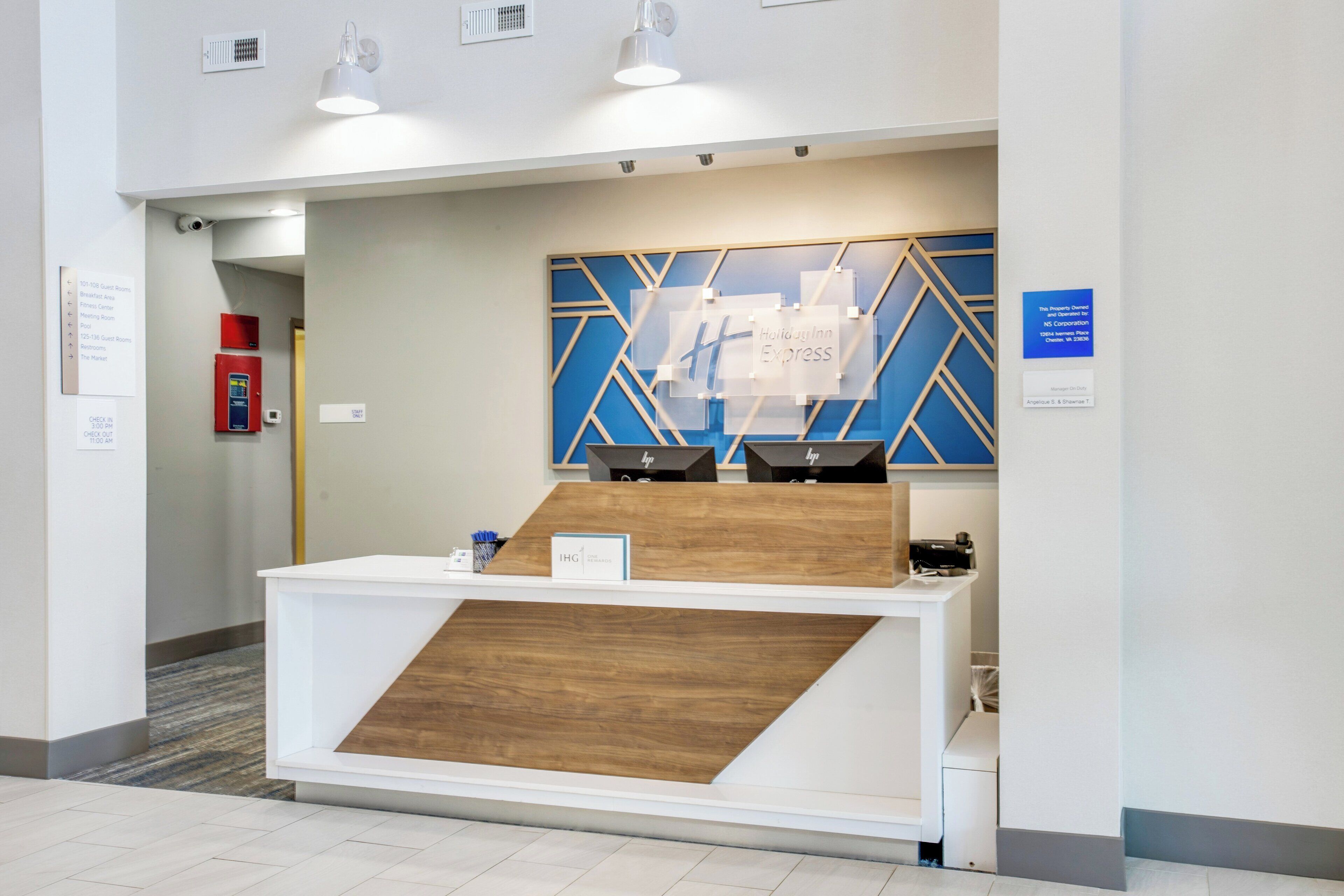 A reception desk with a modern design, a blue geometric wall art, and a sign indicating the location of the hotel lobby.