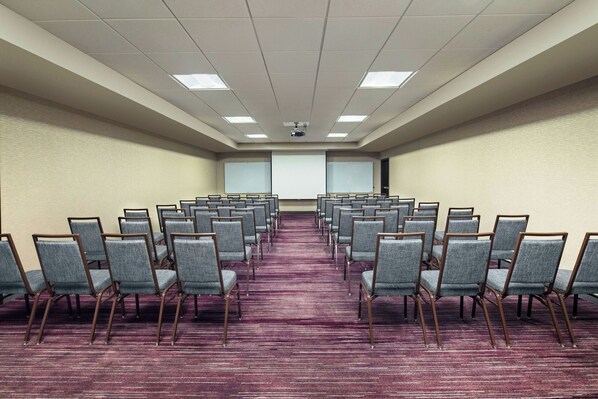 A conference room with rows of chairs, a projector screen, and a carpeted floor.