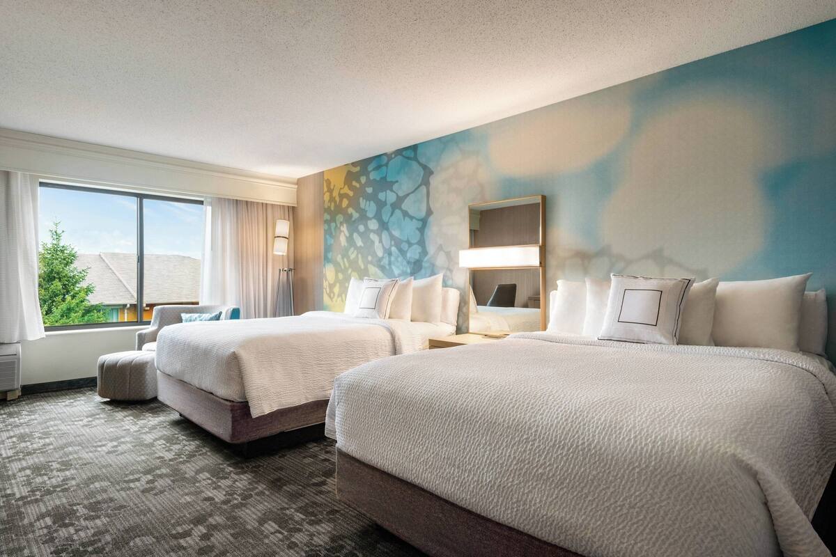 Habitación de hotel con dos camas, un ventanal grande, un cuadro en la pared y vistas al exterior.