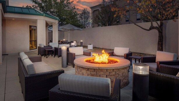 Un área de patio al aire libre con un hogar a leña de piedra rodeado de muebles de mimbre y una mesa de comedor con sillas.