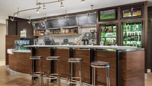 Zona de bar con mostrador de madera, taburetes, una caja registradora y un tablero con la carta.