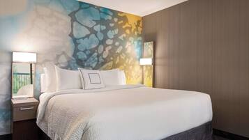 A hotel room with a large bed, two bedside lamps, a nightstand, and a wall with a colorful abstract mural.