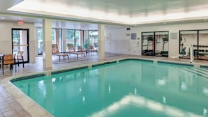 Una piscina interior con agua cristalina, rodeada de sillones de descanso y equipo de ejercicio.