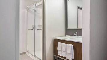 Un baño moderno con cabina de ducha de vidrio, tocador de madera con espejo y lavamanos blanco.