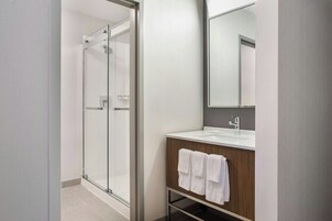 Un baño moderno con cabina de ducha de vidrio, tocador de madera con espejo y lavamanos blanco.