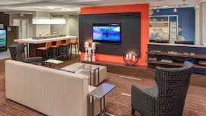 Un vestíbulo de hotel moderno con una zona de bar, asientos y una televisión.