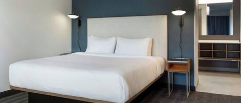 A hotel room with a large bed, a nightstand, a wall-mounted lamp, and a mirror.